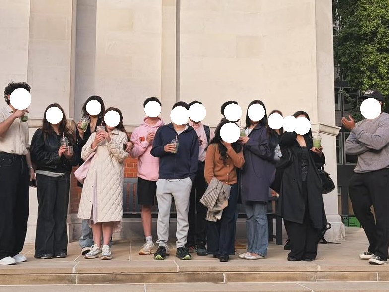 A group of students standing on the steps of a London university building holding matcha drinks, faces masked