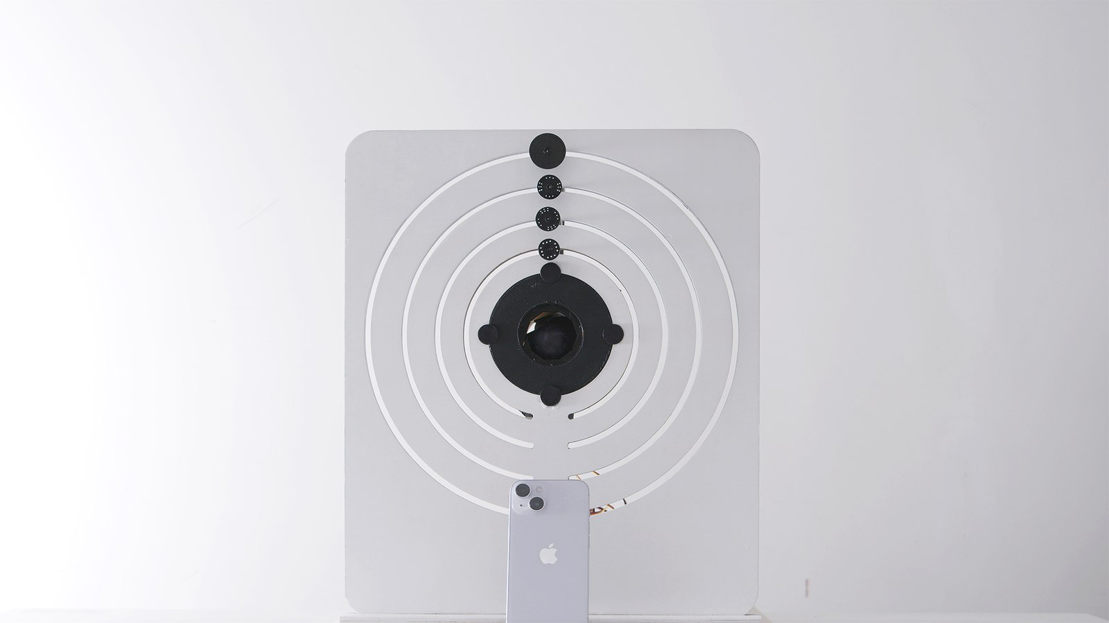 The finished device standing on a white surface: a square panel with concentric rings, a dark iris at the centre and small black markers at ring positions