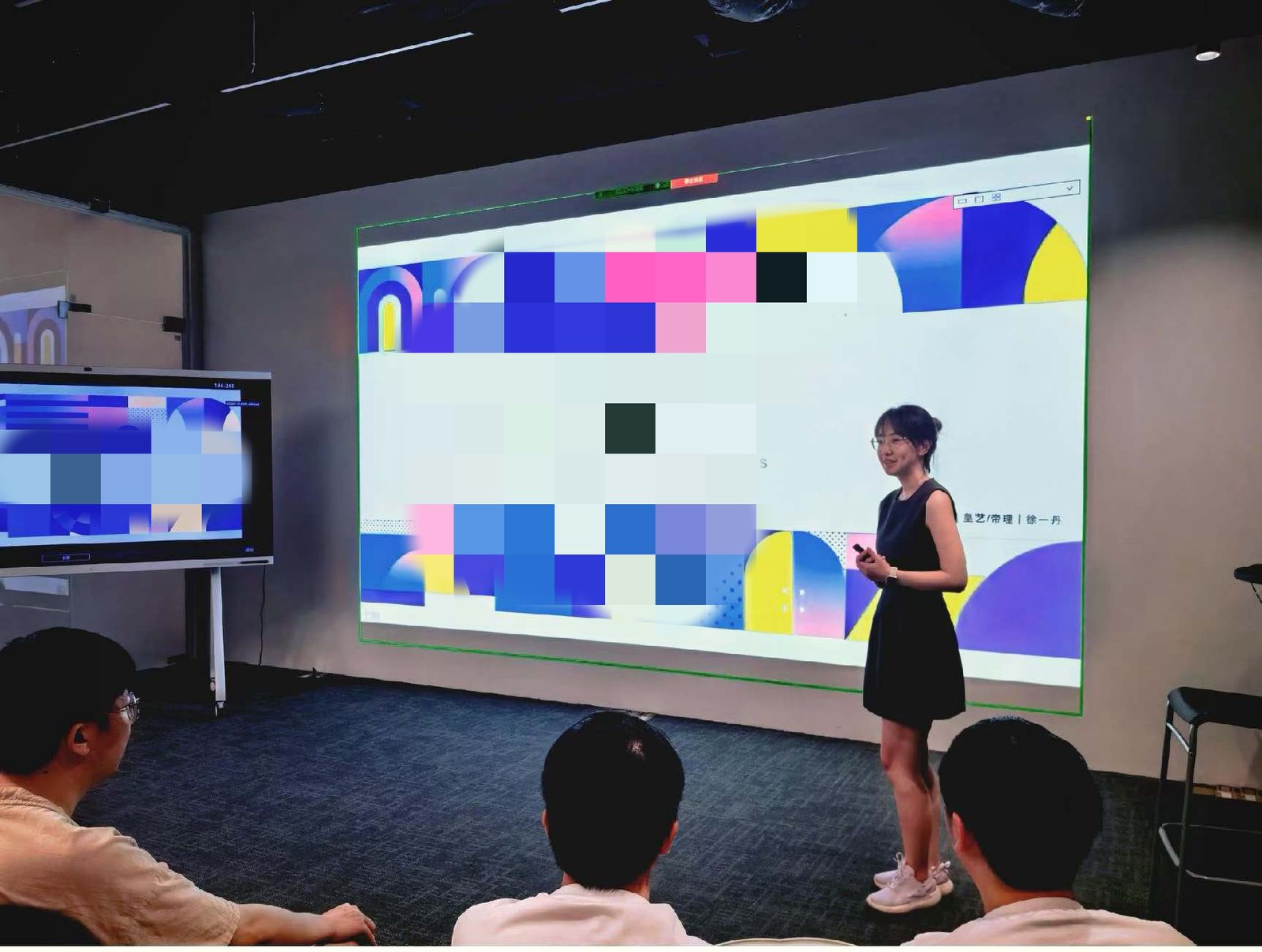Yidan Xu presenting to colleagues in a Huawei meeting room, standing beside a large projected slide whose content is pixelated, with three people watching from the front row