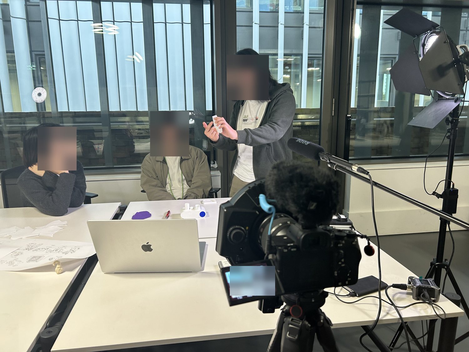The workshop being filmed: two participants at a table covered in sketches and torn paper cards, with a facilitator standing and holding a white prototype of the RES sensor, a camera and boom microphone set up in front of them