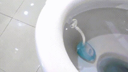 The Urify tablet clipped under the rim of a toilet. It goes in pale blue, and by the end of the clip the water running past it has turned it green