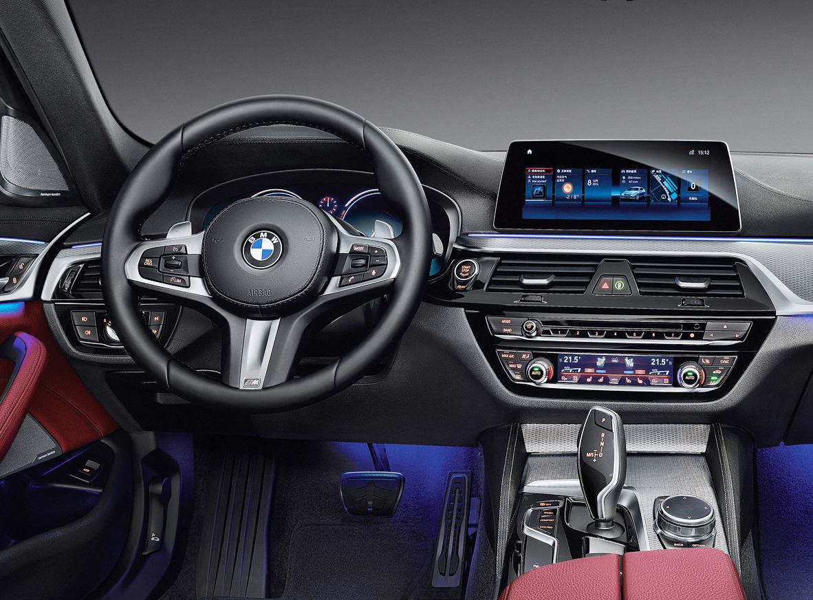 The interior of a petrol saloon: a screen high on the dashboard, and below it two rows of physical buttons and dials for climate and media, plus a rotary controller by the gear selector