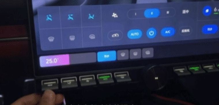A hand at the left end of the physical strip. On the screen the climate bar shows the driver's temperature falling, highlighted on the left-hand side